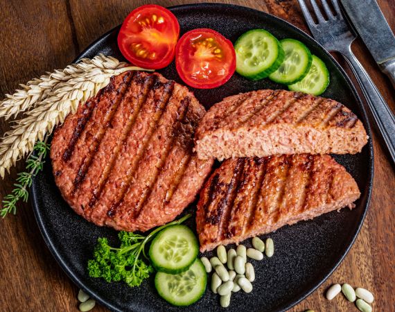 Pflanzenbasierte Burge-Patties auf einem schwarzen Teller mit Gurken- und Tomatenscheiben