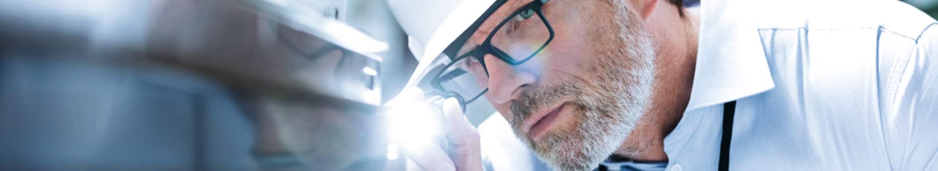 Mann mit schwarz gerahmter Brille und Sicherheitshelm leuchtet mit Taschenlampe