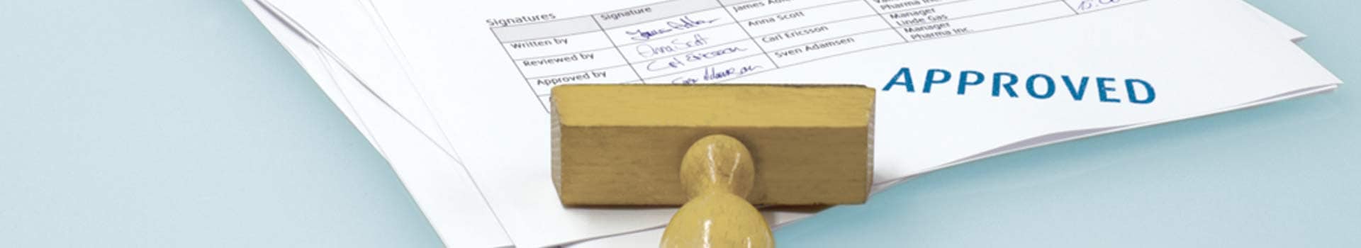 Stempel liegt auf Papierstapel auf dem Approved steht