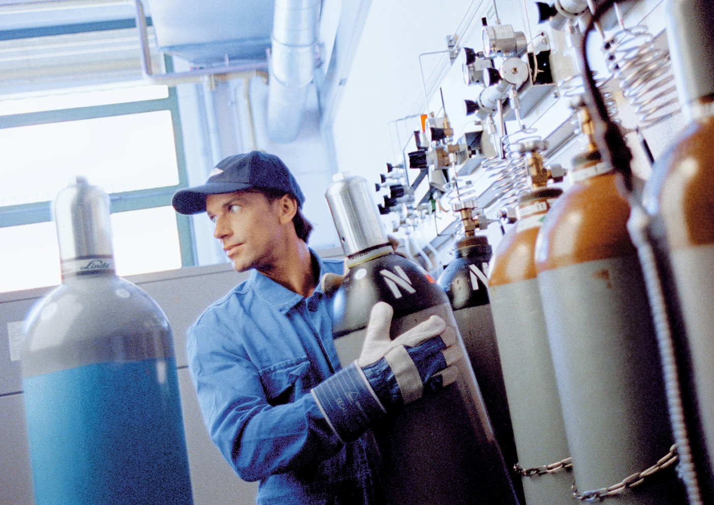 Operatore in abbigliamento tecnico che movimenta bombole industriali in un impianto di gas