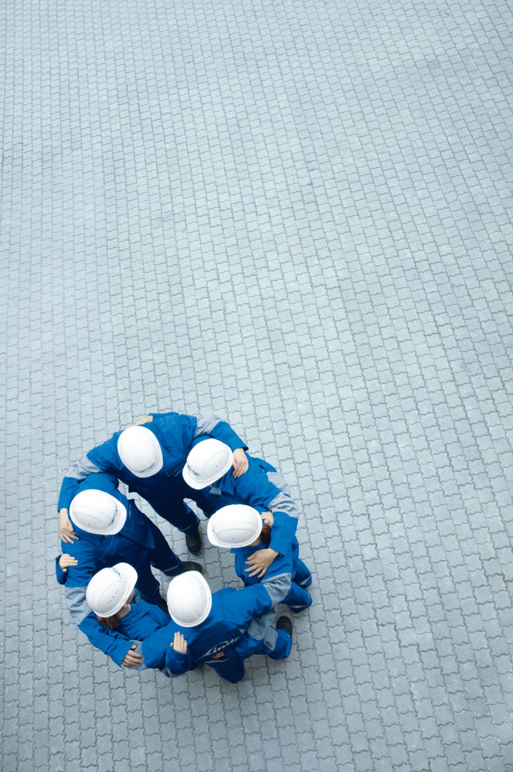 Squadra di lavoratori con caschi protettivi riunita in cerchio su una pavimentazione industriale