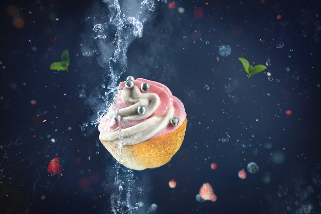 Een half bevroren cupcake met zwevende aarbeien in de achtergrond